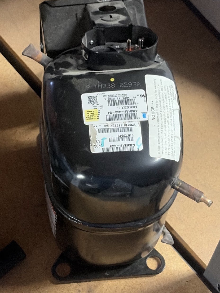 A hermetic reciprocating compressor on a bench.